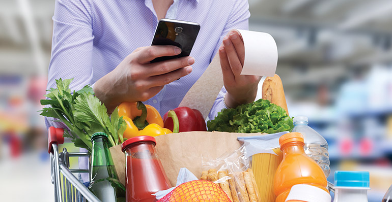 Someone holding a grocery bill, using a phone, in front of produce.