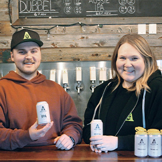 A photo of Keegan Padyk and Bridget Atkinson Fee posing with Anderson Ales beer cans