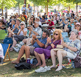 Photo of an audience sitting on a lawn at Home County