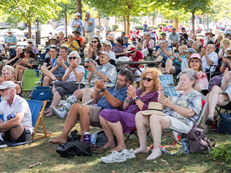 Photo of an audience sitting on a lawn at Home County