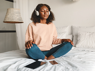 A stock image of a woman meditating while wearing headphones.